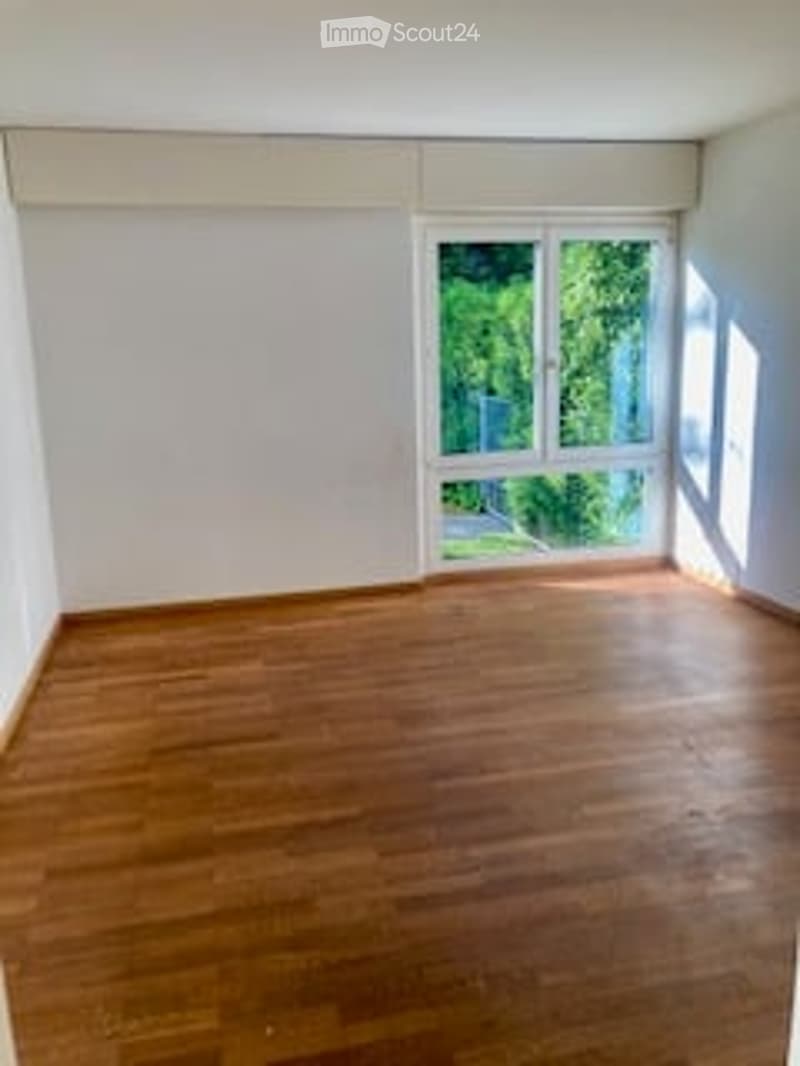 Completely empty room with wooden flooring and large windows, allowing natural light to fill the space.