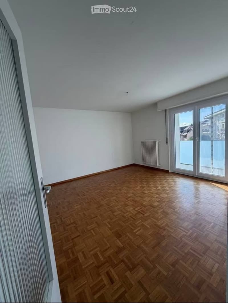 Empty room with wooden parquet flooring, white walls, and large sliding glass doors leading to a balcony.