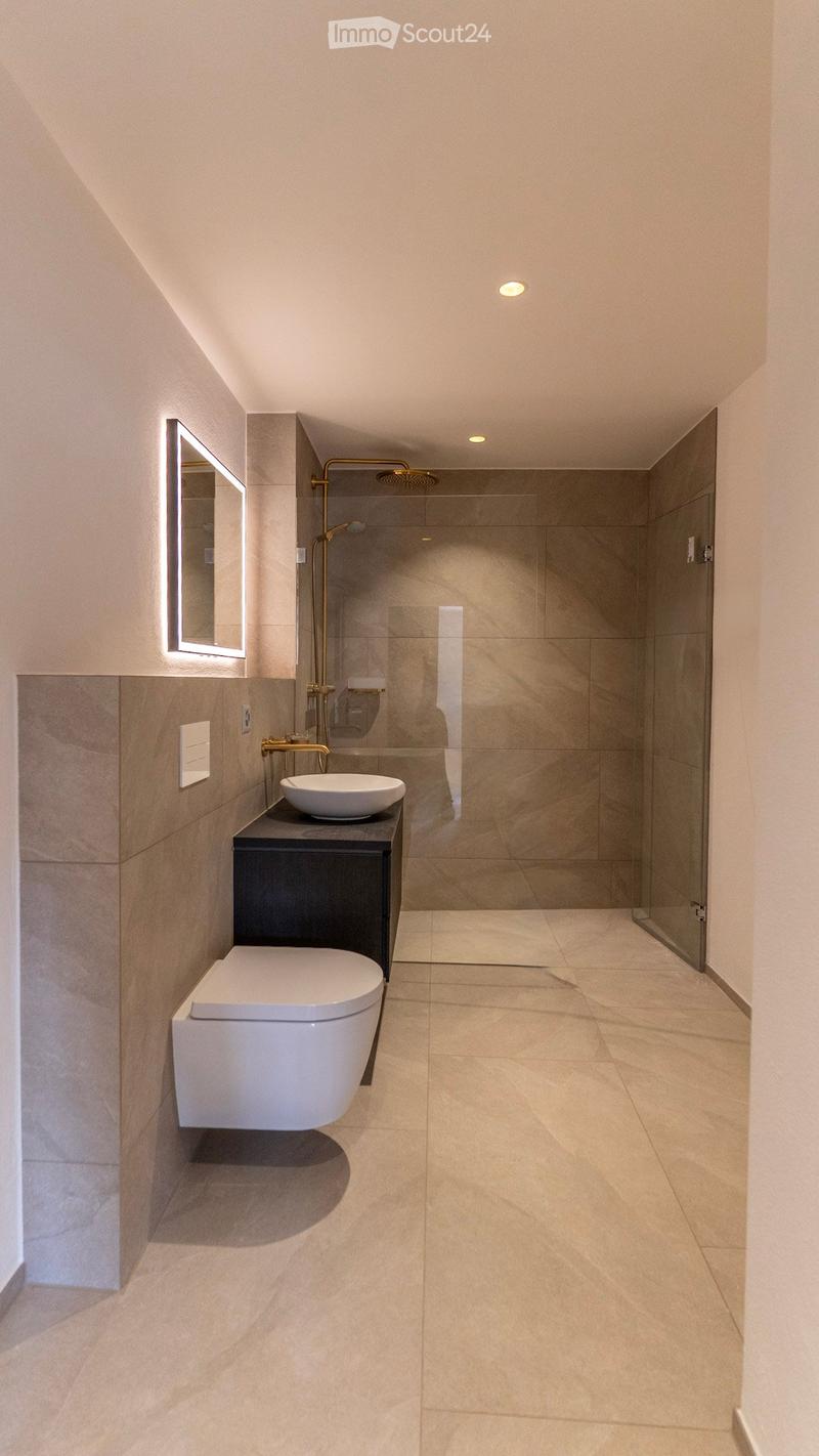 Modern bathroom with a toilet, sink, mirror, and glass-enclosed shower area. Light-colored tiles and sleek fixtures.