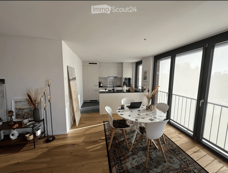 Open-plan living and dining area with modern furniture, large windows, and a sleek kitchen in the background.
