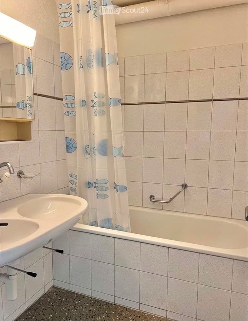 Bathroom with white tiled walls, a double sink, a bathtub with a shower curtain, and a mirror above the sink.