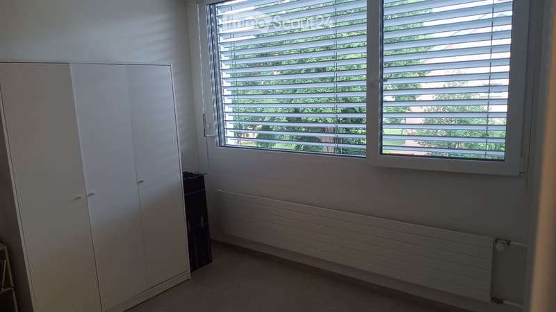 Empty room with white walls, large window with blinds, radiator, and a closet.