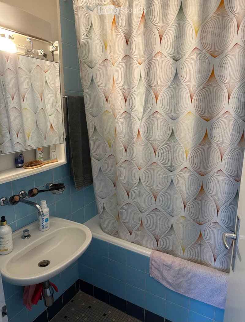 Bathroom with blue tiles, a white sink, a bathtub with a decorative shower curtain, a mirror, and a towel on the edge of the tub.