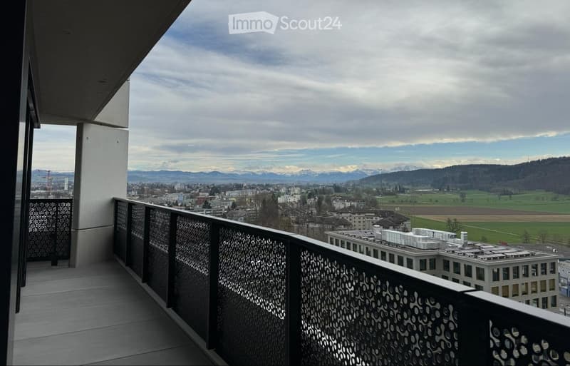 Balcony with a modern metal railing, overlooking a cityscape and distant mountains under a partly cloudy sky.