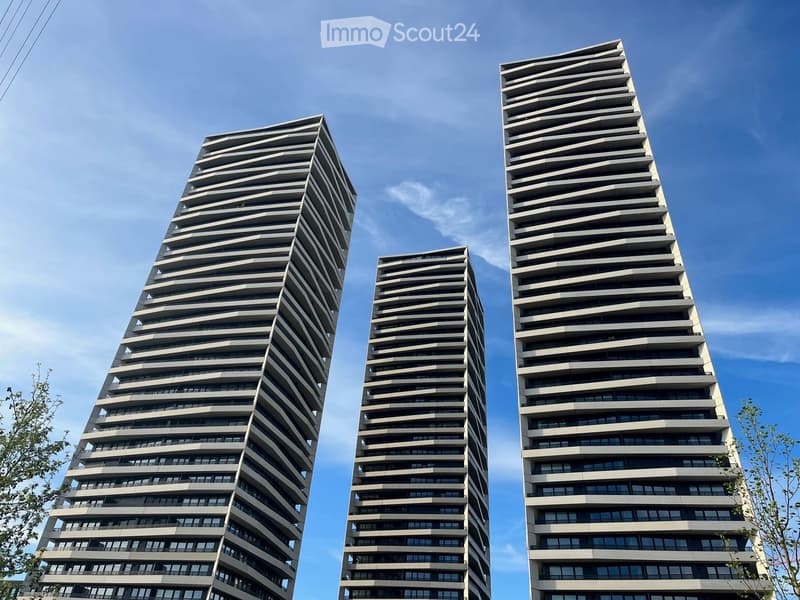Four modern high-rise buildings with a sleek, tiered design and numerous windows, set against a clear blue sky.
