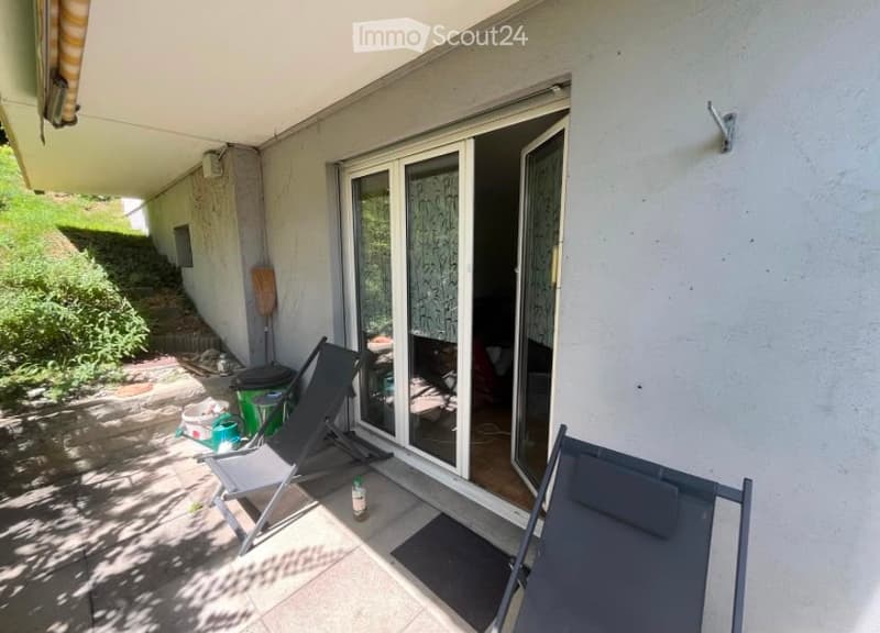 Balcony with sliding glass doors, two lounge chairs, and a small storage area with a broom and trash bins.