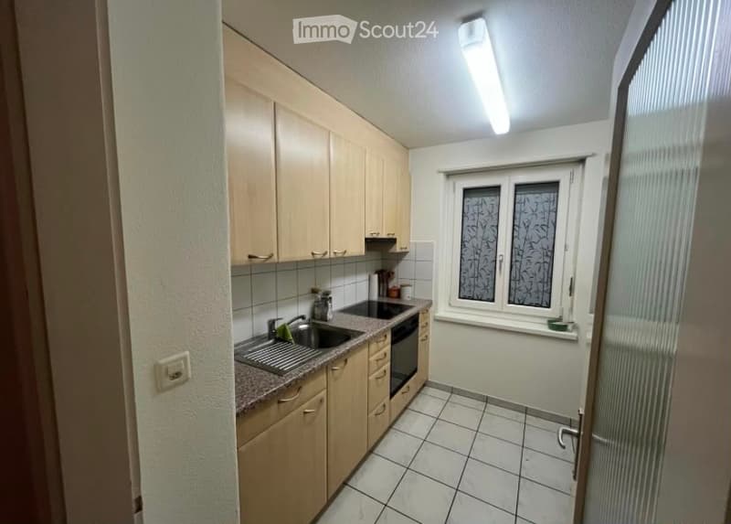 Modern kitchen with light wooden cabinets, tiled floor, sink, oven, and window with decorative glass.