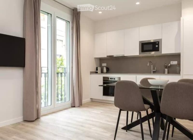 Modern, well-lit kitchen and dining area with white cabinets, stainless steel appliances, a dining table with chairs, and large windows leading to a balcony.