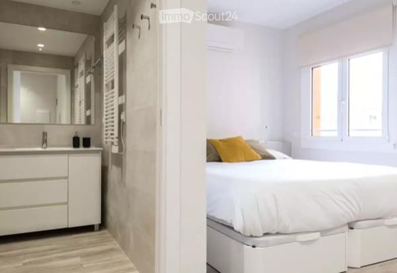 Modern bedroom with a white bed, yellow pillows, and a sleek bathroom area featuring a mirror and sink.