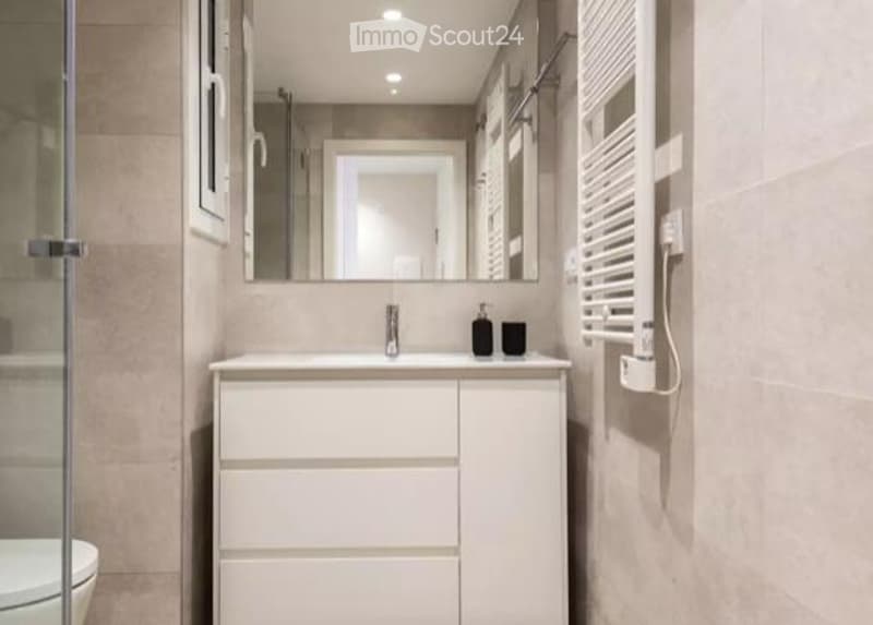Modern bathroom with a white vanity, sink, mirror, and a glass-enclosed shower area.