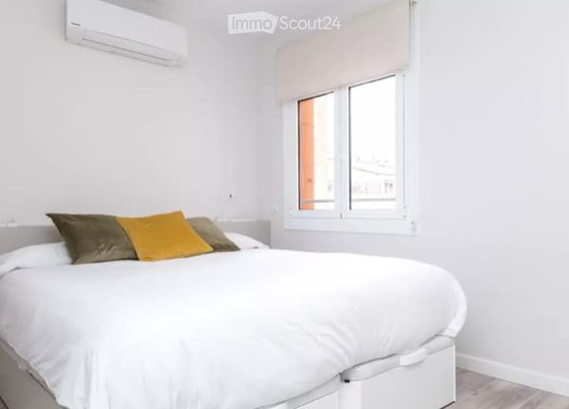 Modern bedroom with a large bed, multiple pillows, a window with blinds, and an air conditioner mounted on the wall.