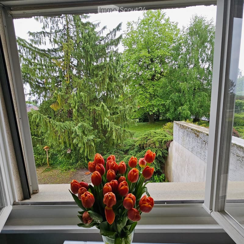 A window view shows a garden with lush green trees and a cluster of red tulips in a vase on the windowsill.