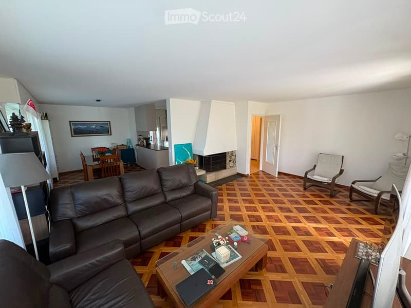 Living room with a dark brown leather sofa, coffee table, wooden dining table, fireplace, and several chairs.