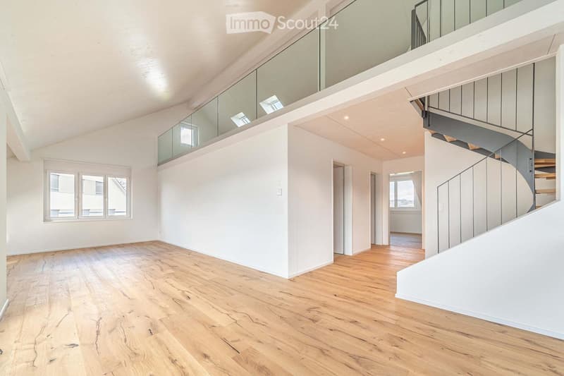 Bright, open-plan space with wooden flooring, white walls, large windows, and a modern glass balcony railing. No furniture or equipment present.