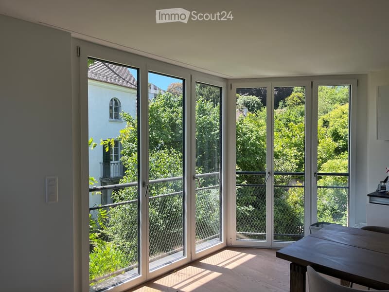 Bright room with large sliding glass doors leading to a balcony, wooden floor, and a small table and chair near the balcony.