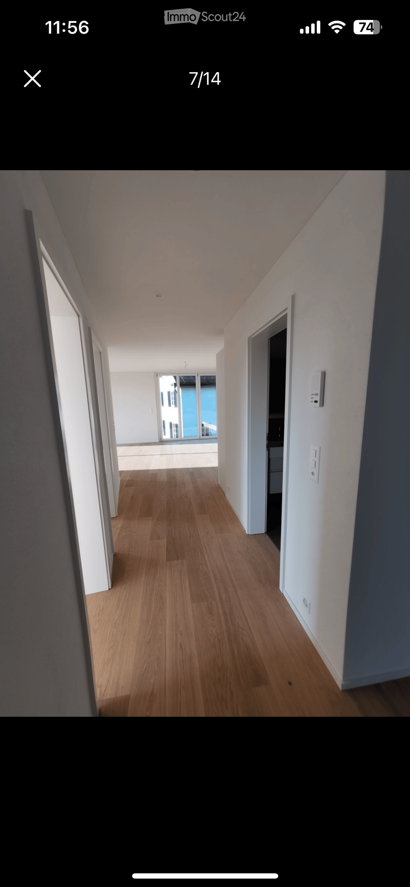 Empty hallway with wooden flooring, white walls, and multiple doors leading to other rooms.