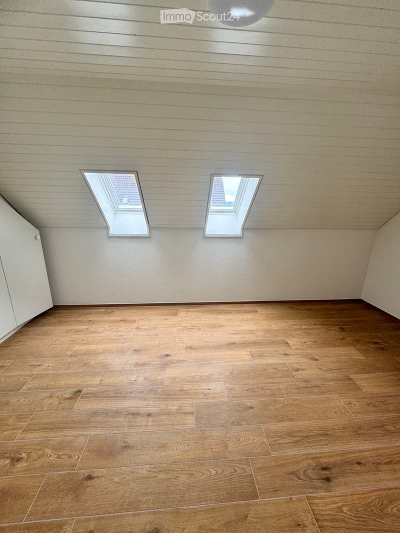 Empty room with wooden flooring and two skylight windows in the ceiling.