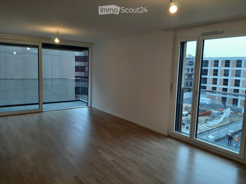 Empty room with wooden flooring, large windows, and sliding glass doors leading to a balcony.