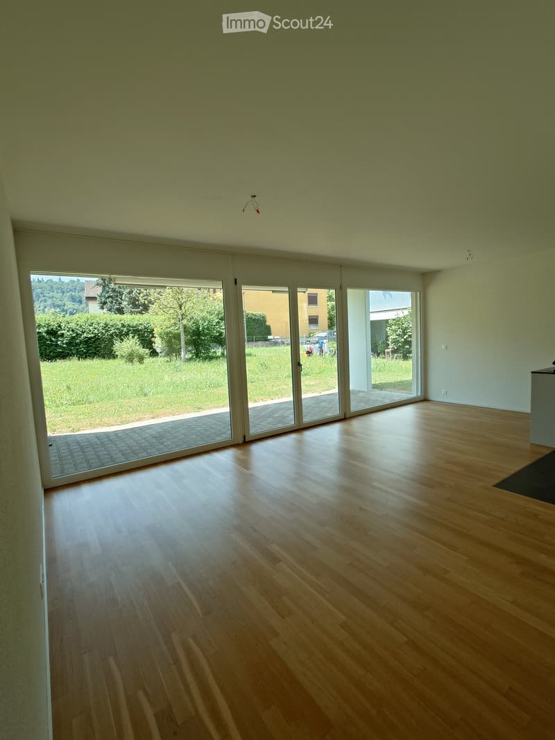 Empty room with light wooden flooring, large sliding glass doors leading to a grassy outdoor area, and white walls.