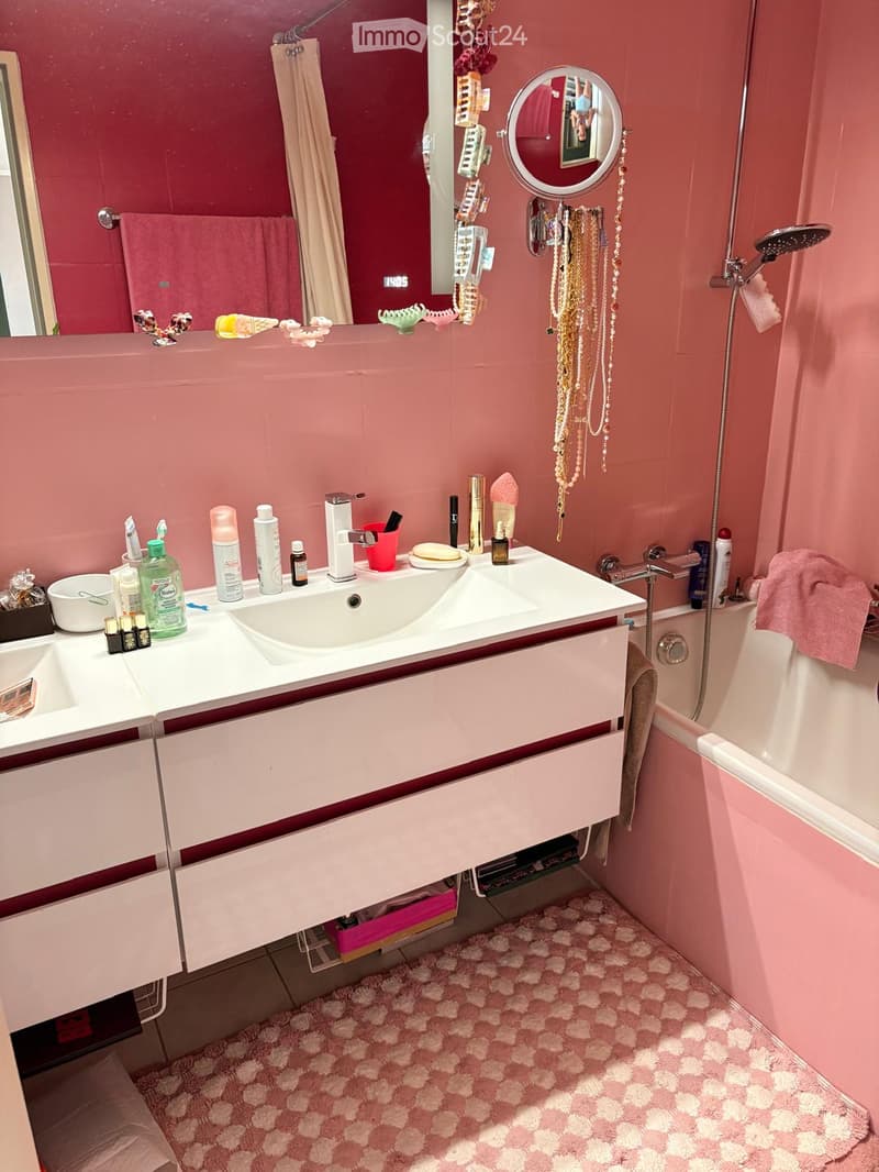 A pink-themed bathroom with a double sink vanity, a bathtub, a large mirror, and various toiletries and decorative items.