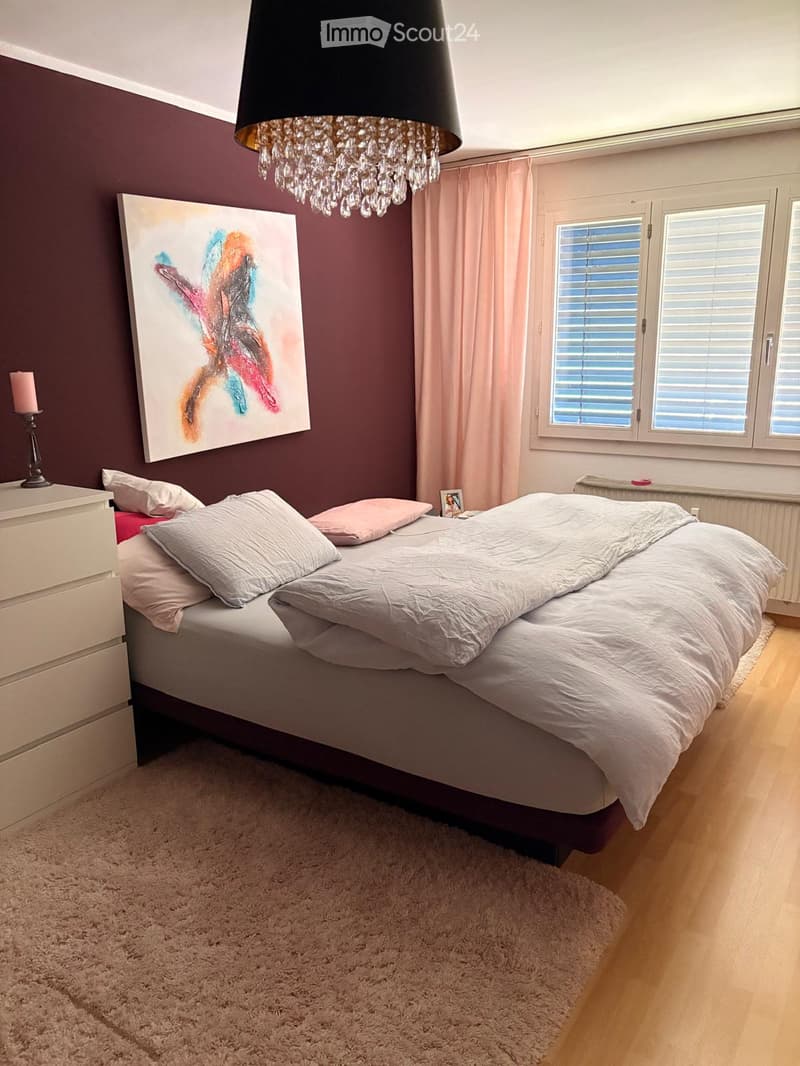 A modern bedroom with a large bed, white bedding, nightstand, chandelier, and artwork on the wall.