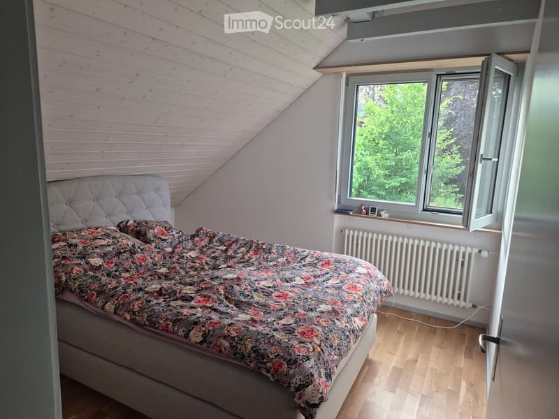 Cozy attic bedroom with wooden slanted ceiling, large windows, and a floral bedspread.