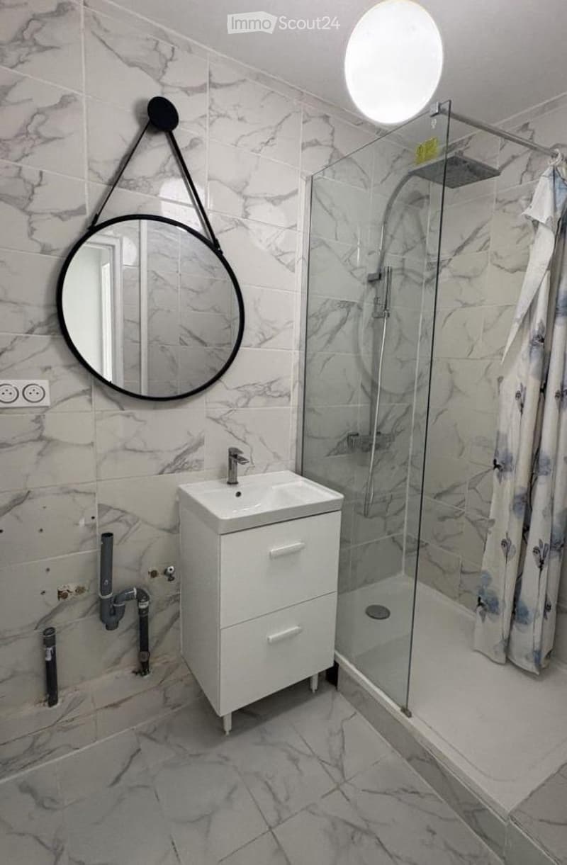 Modern bathroom with marble tiles, white sink cabinet, round mirror, and glass-enclosed shower.