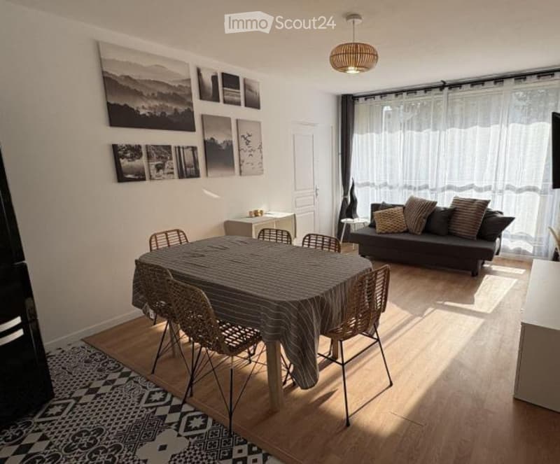 Bright, modern living and dining area with a sofa, dining table, chairs, side table, floor lamp, and picture frames on the wall.