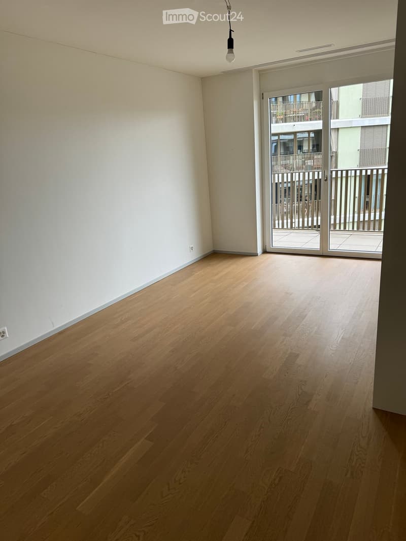 Empty room with wooden flooring, white walls, and a sliding glass door leading to a balcony.