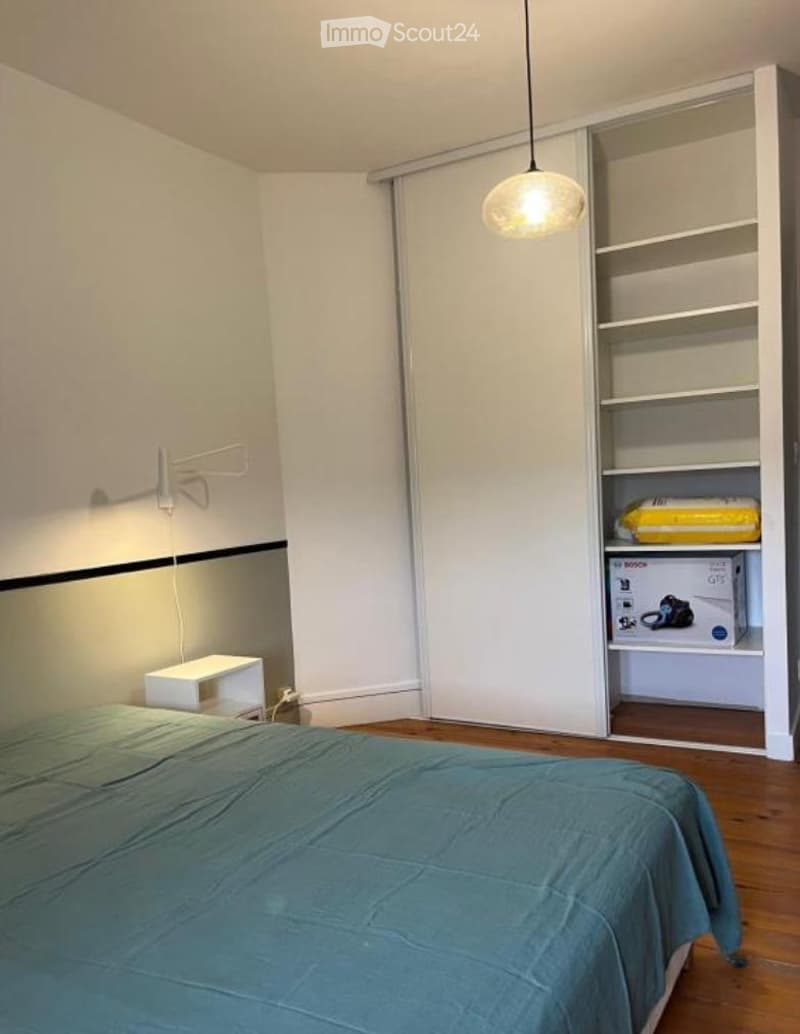 A modern bedroom with a neatly made bed, a nightstand, a built-in wardrobe with shelves, and a hanging pendant light.