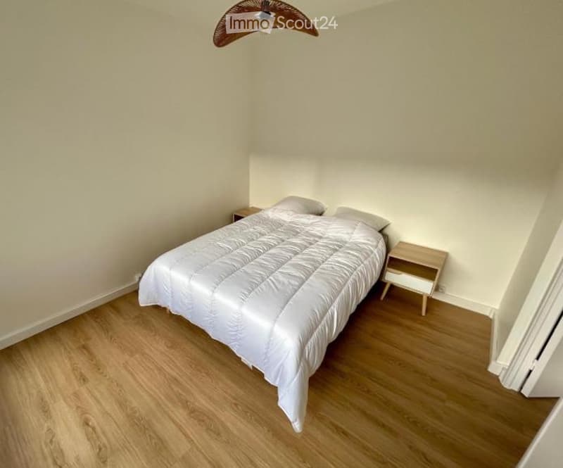 Cozy bedroom with a white duvet-covered bed, wooden nightstands, and a hanging wooden ceiling light.