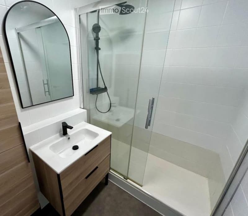 Modern bathroom with a white tiled shower stall, a wooden vanity with a sink, and a large oval mirror.