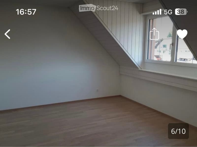 Empty attic room with wooden flooring, white walls, and a large window offering a view of the outside.