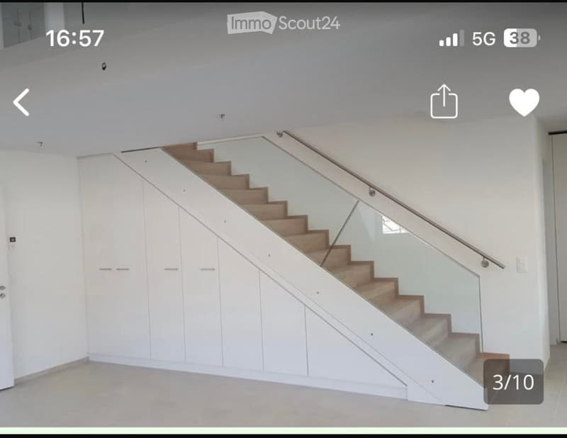 Modern staircase with wooden steps and glass railing, white built-in storage cabinets on one side, light-colored walls and floor.