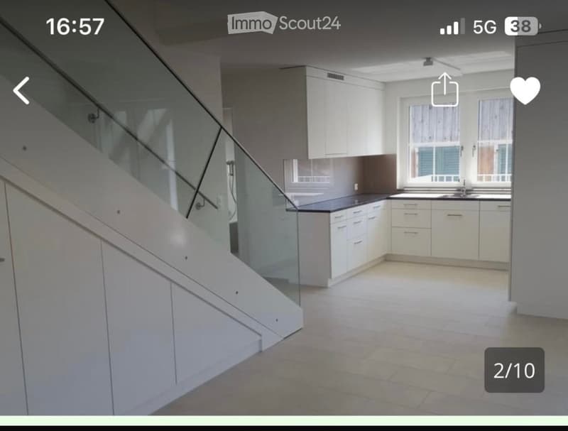Empty kitchen with white cabinets, black countertops, and a staircase with a glass railing leading upwards.