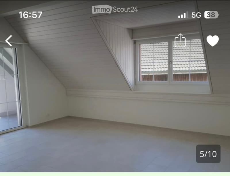 Empty attic room with slanted ceilings, large window, and tiled floor. No furniture or equipment present.