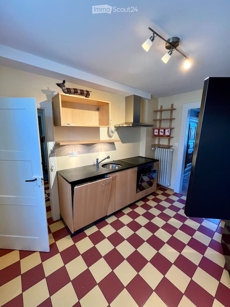 Modern kitchen with wooden cabinets, black countertop, sink, faucet, oven, and range hood. The floor features a red and yellow checkered pattern.