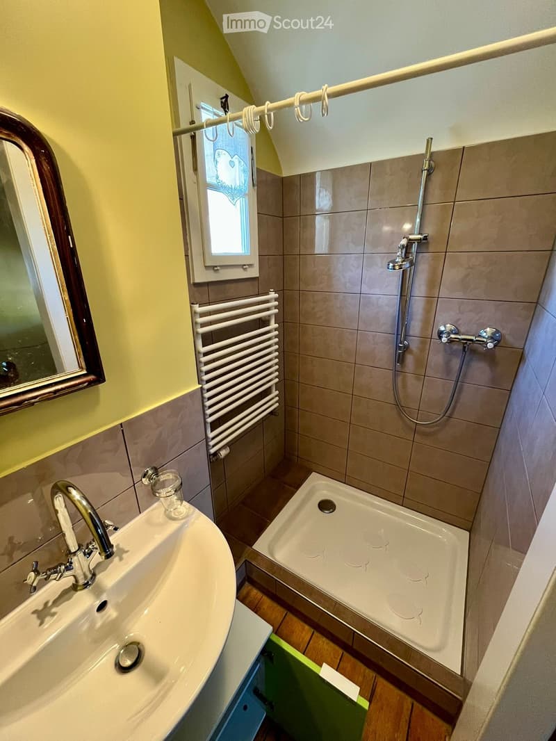 Bathroom with a sink, mirror, bathtub, shower, radiator, and a small window with a decorative curtain.