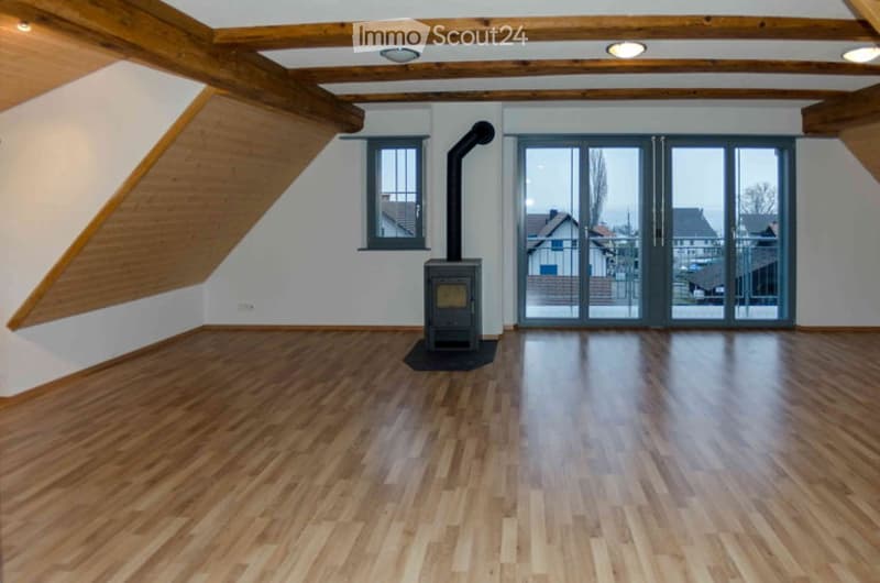 Empty room with wooden floor, exposed wooden beams, fireplace, large window, and sliding glass doors leading to a balcony.