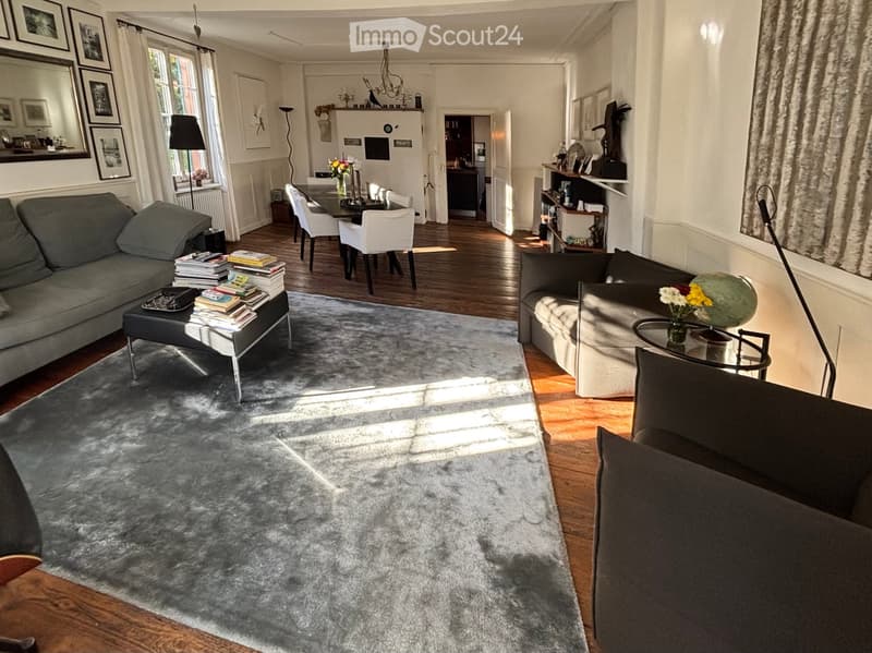 open plan living room and dining area, gray couch, glass center table, carpet, floor lamp, round table and chairs, wooden floors, chandelier