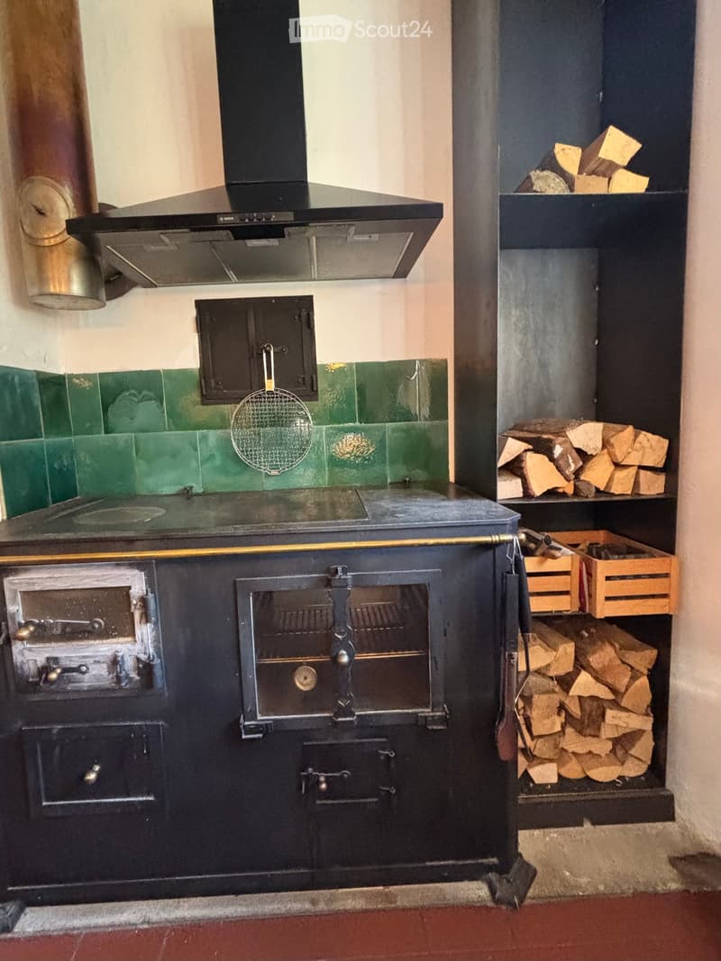 Traditional wood-burning oven and chimney, green tiled wall, wooden crate, and wooden logs