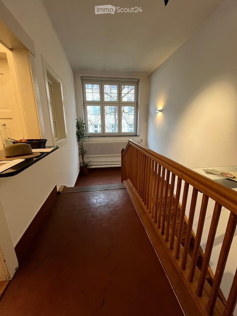 raised ground floor, wooden staircase, tiled floor, window with view to outside, radiator, plant, and light fixture
