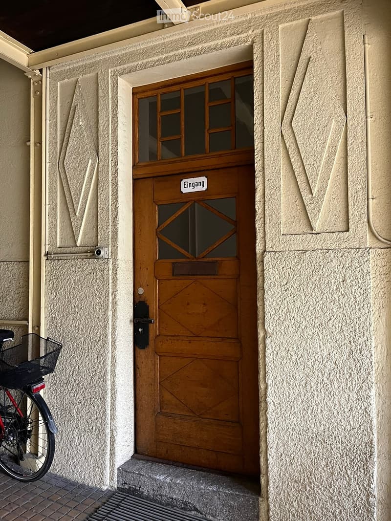 Wooden door with glass panel, label 'Eingang', gray stone wall, mailbox, bicycle parked on left