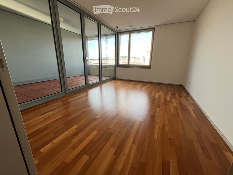 Empty room with wooden flooring, large windows, and sliding glass doors leading to a balcony.