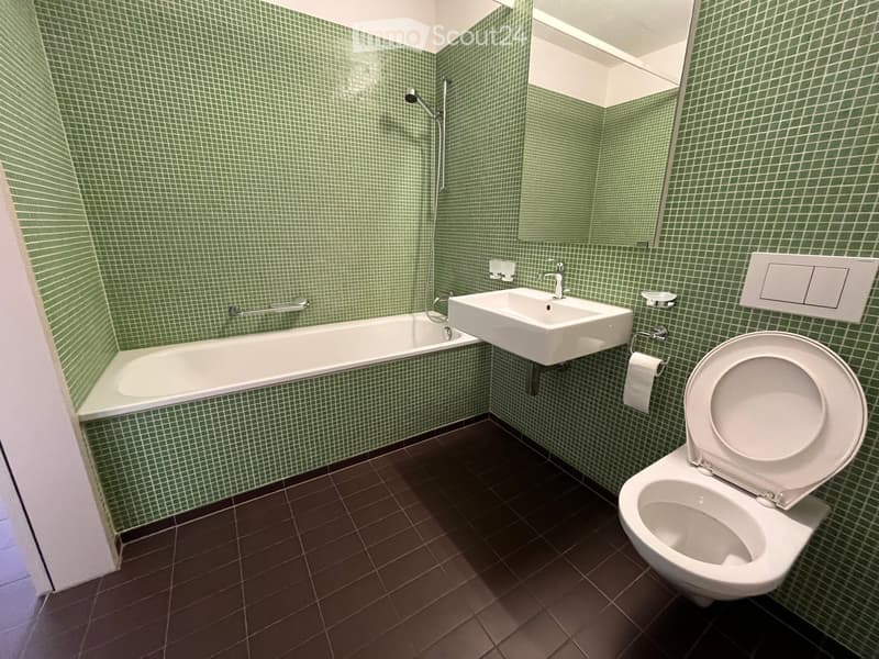 Bathroom with green tiled walls, bathtub, sink, toilet, and a mirror above the sink.