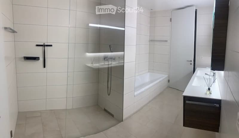 Modern bathroom with white tiles, a bathtub, a sink, a large mirror, and a glass-enclosed shower area.