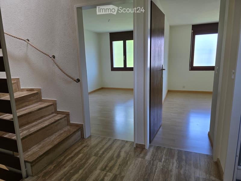 Empty hallway with wooden flooring, a staircase leading upwards, and two open doors leading to adjacent rooms.