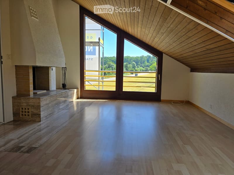 Empty room with wooden flooring, a fireplace, and large windows offering a view of the outdoors.