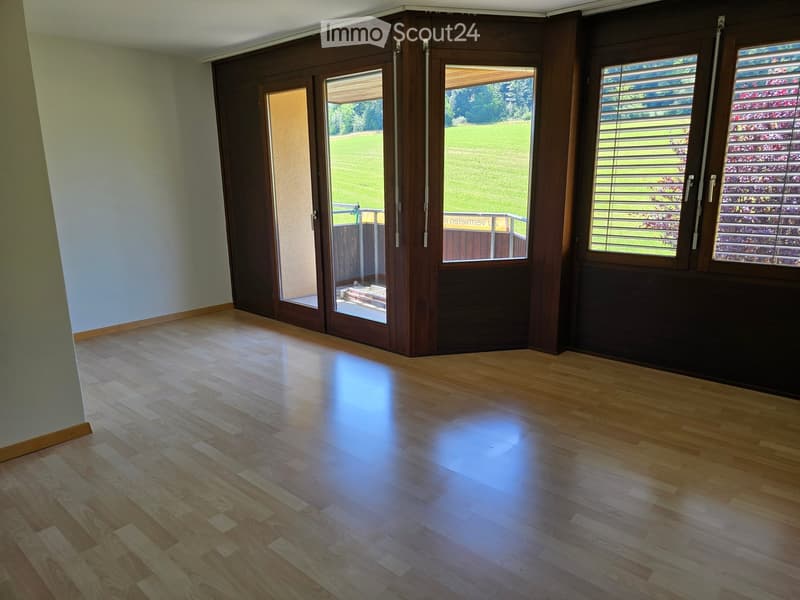 Empty room with wooden flooring, large sliding glass doors leading to a patio, and windows with blinds.