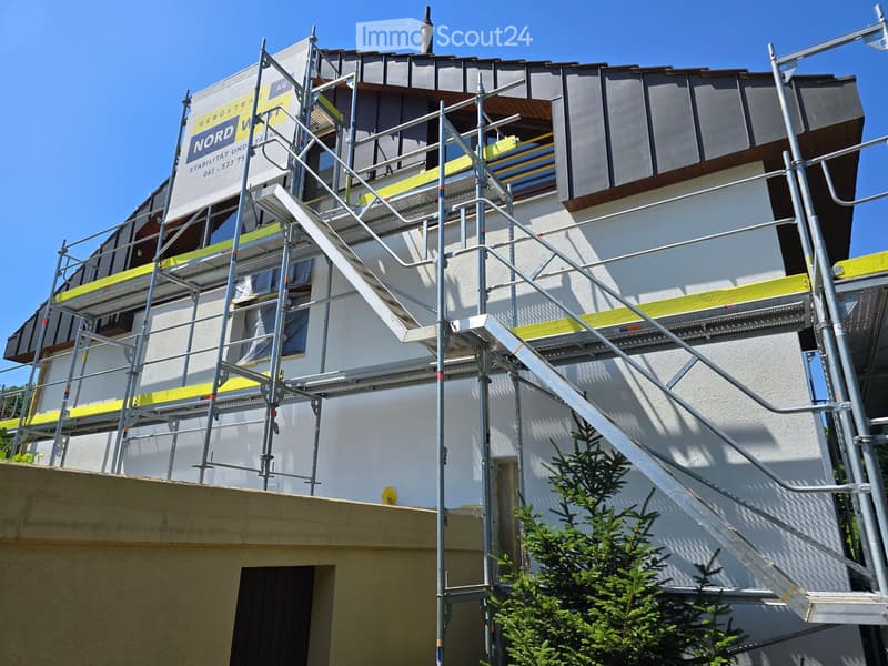 A multi-story building under construction with scaffolding, metal railings, and a partially covered roof.
